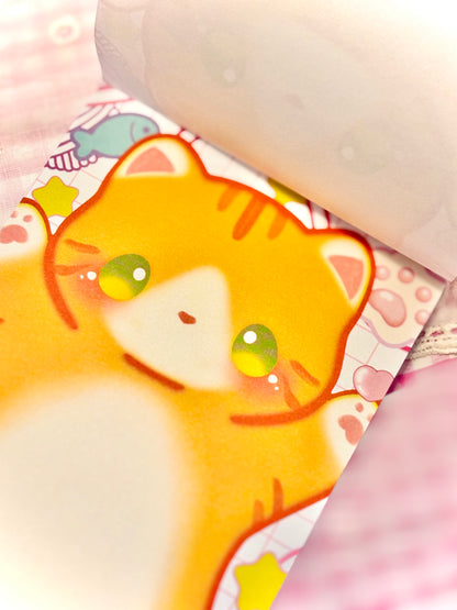 A close-up of a pastel pink and white patterned notebook or journal page featuring a cute orange tabby cat illustration, with a rolled page visible at the top.