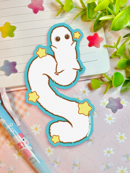 A cute cartoon worm sticker with a turquoise outline and yellow stars, placed on a pink floral notebook with a pen and green leaves in the background.